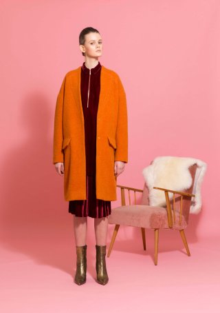 Model mit orangenem Mantel vor rosa Hintergrund