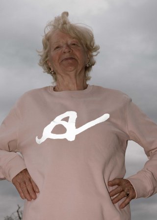 Model mit kurzen blonden Haaren in einem pastellrosa Pullover mit weißem Buchstaben