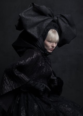 Model in ausgefallenem schwarzen Outfit vor schwarzem Hintergrund